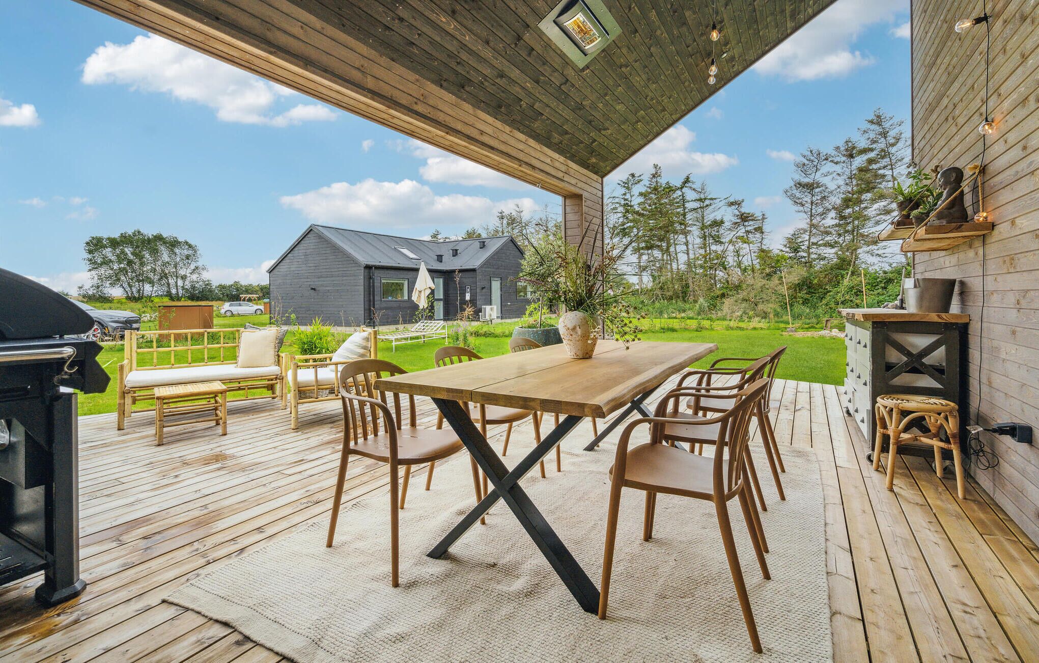 An outdoor deck with a wooden table and chairs, a grill, and a potted plant.