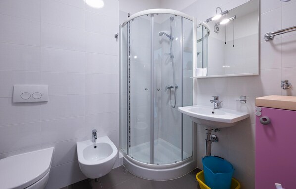A modern bathroom with a glass-enclosed shower, a bidet, a sink, and a toilet.