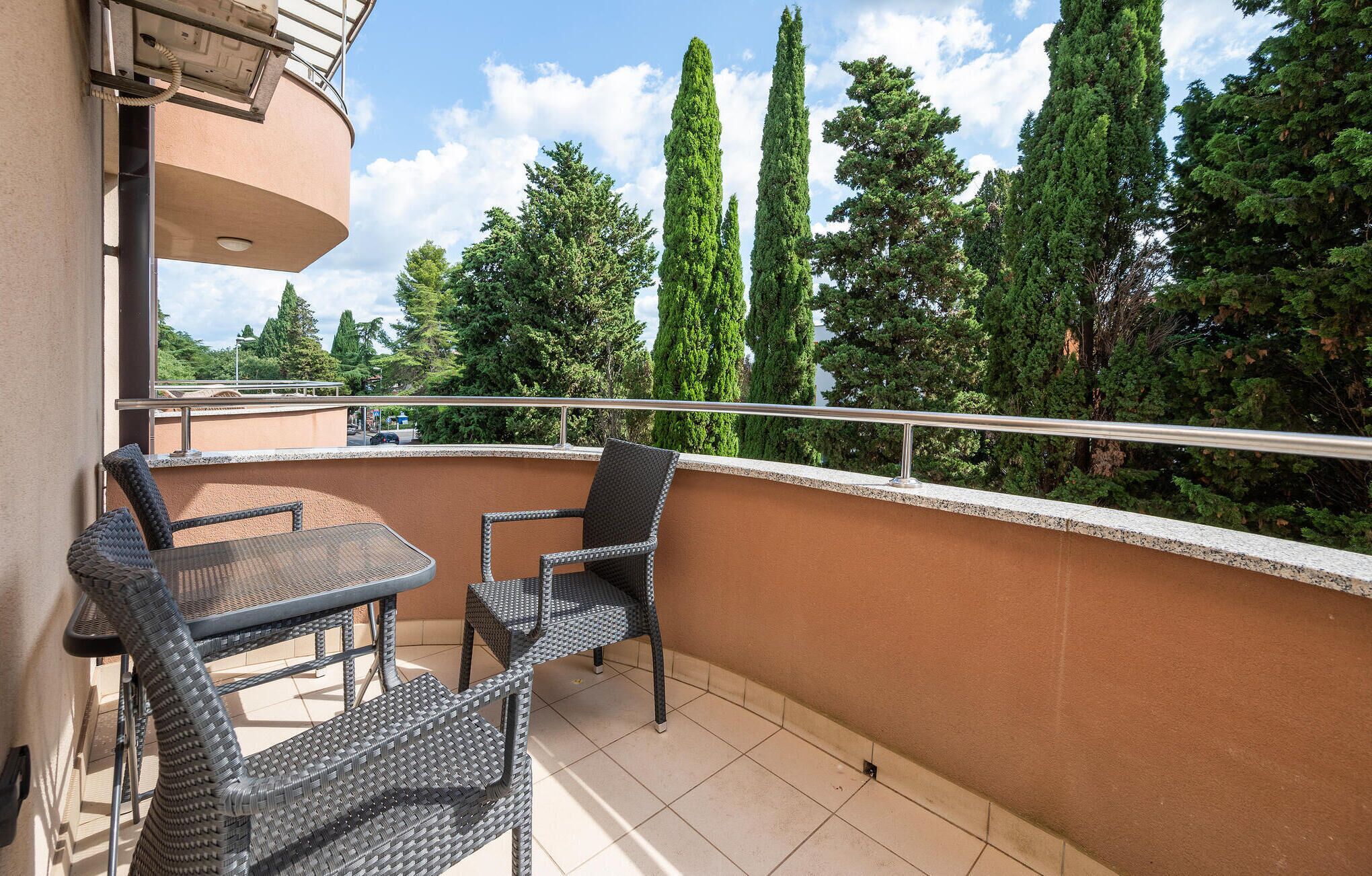 A balcony with wicker furniture, a view of tall trees, and a clear sky.