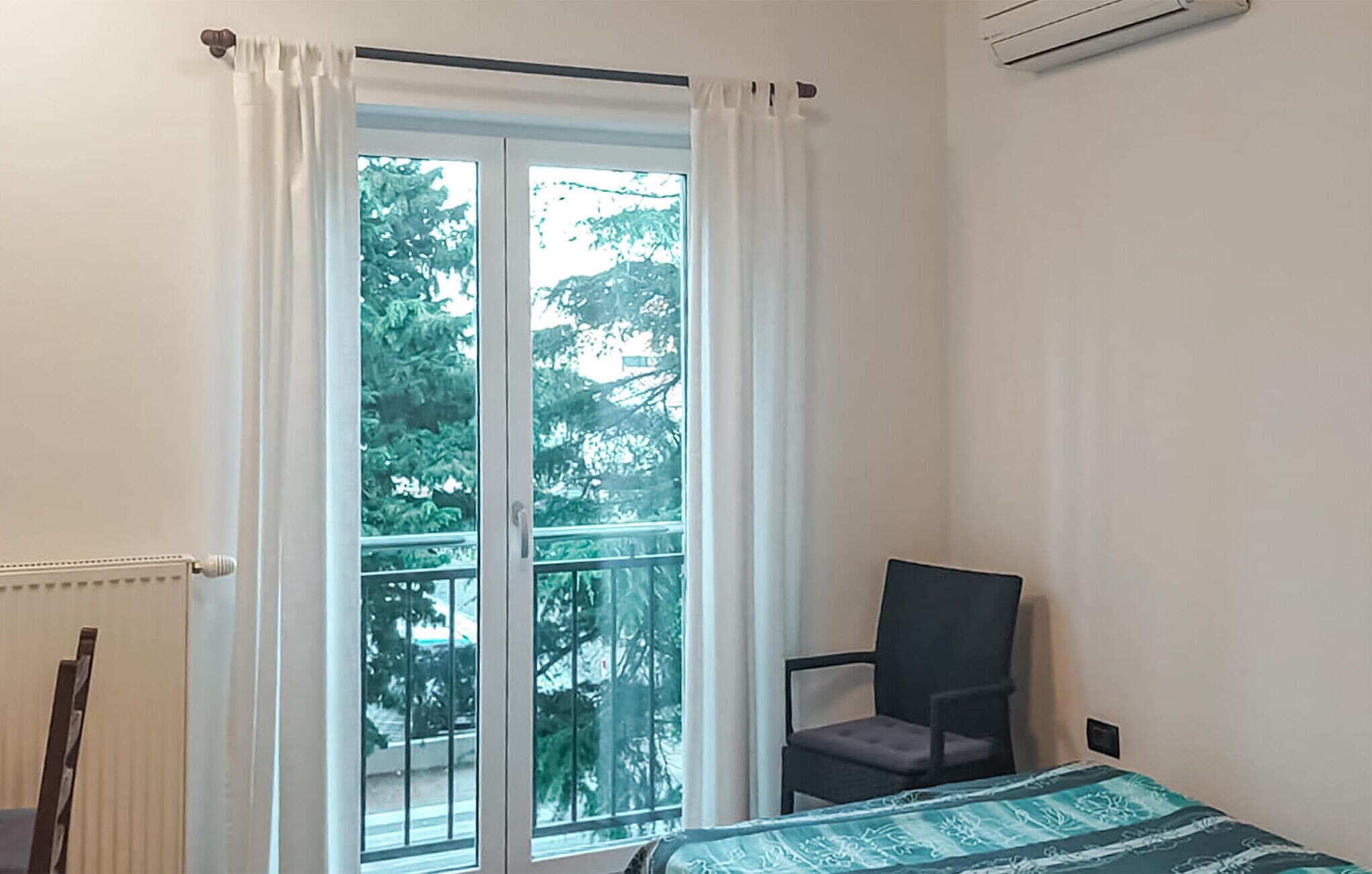 Una habitación con cama, una silla y un ventanal con cortinas.
