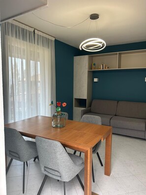 A modern dining area with a wooden table and grey chairs, a sofa, and a ceiling light fixture.