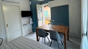 Quarto com cama, escrivaninha e cadeira. Há uma televisão na parede e um aparelho de ar condicionado sobre a cama.