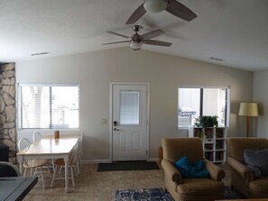 A room with a dining table, chairs, a sofa, a floor lamp, a ceiling fan, and a door.