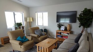 Ein Wohnzimmer mit einer Couch, Sesseln, einem Couchtisch, einem Fernseher und einem Bücherregal.