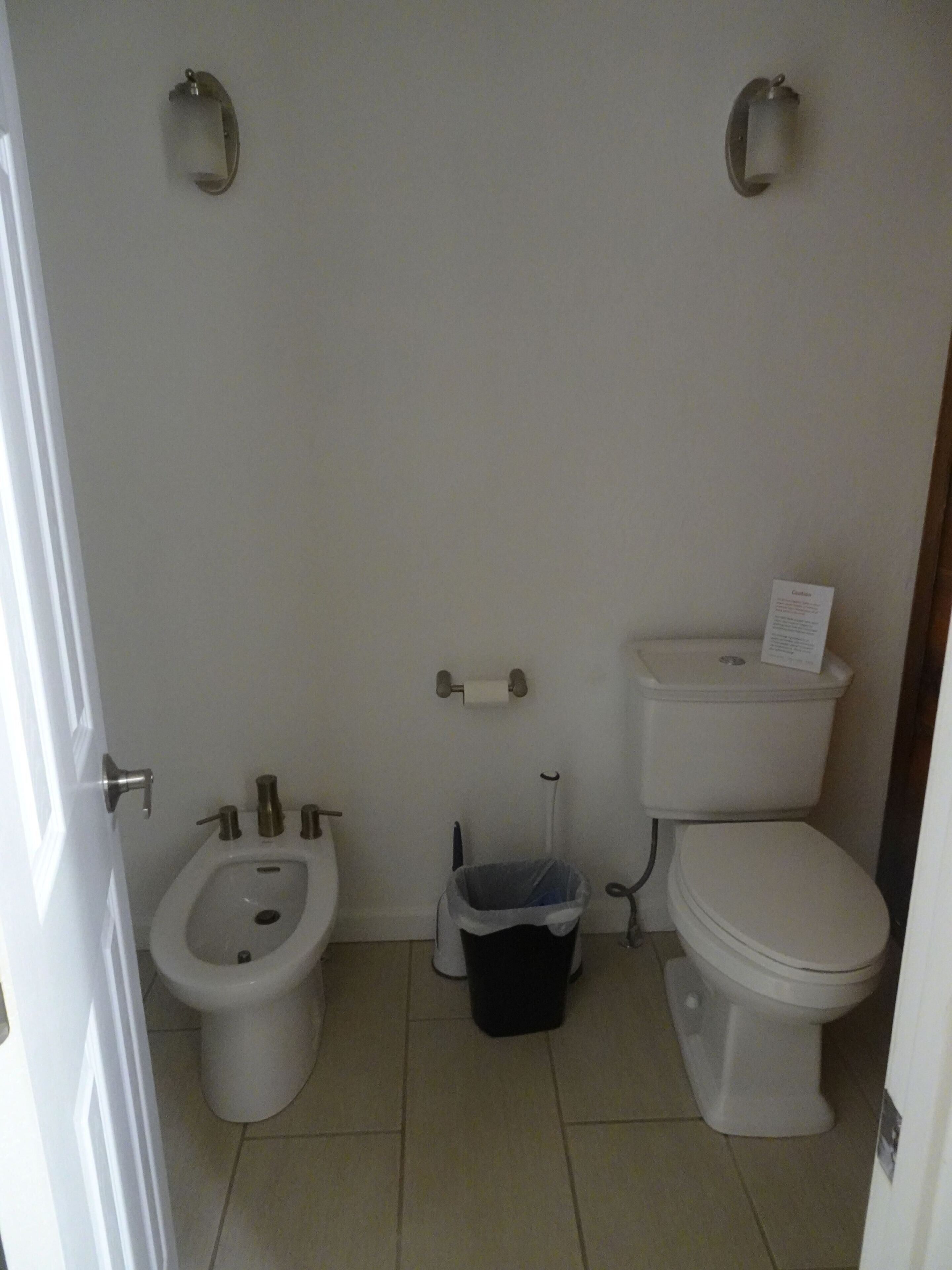 A small bathroom with a toilet, bidet, and trash can.