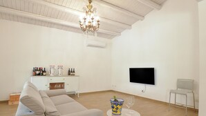 A spacious living room with a sofa, a television mounted on the wall, a wine bottle, and a glass on a small table. - Stunning home in Menfi (Menfi)