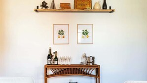 A modern living room with two white sofas, a wooden coffee table, a wicker side table with wine glasses, and a bookshelf with decorative items. - Cozy 2BR/2BA Apt on Broadway (Newport)