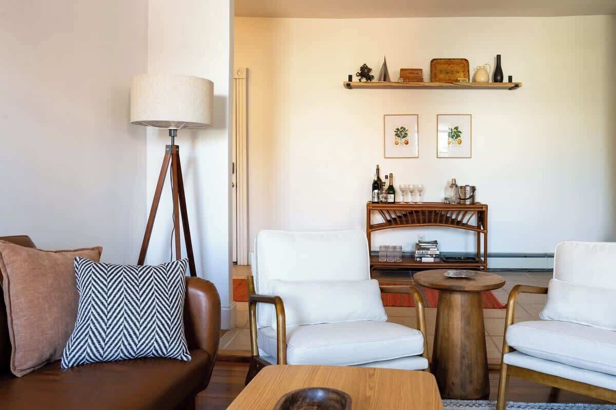 Una sala de estar con un sofá marrón, un sillón blanco, una mesa de centro de madera y una lámpara de pie.