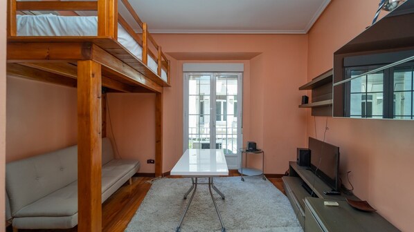 Habitación pequeña con una cama litera, un sofá, una mesita y un televisor.