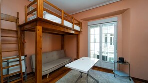 Habitación con literas, un sofá, una mesa y una ventana que da a edificios.