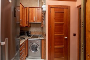 Una cocina compacta con armarios de madera, un refrigerador de acero inoxidable, una lavadora y un microondas.