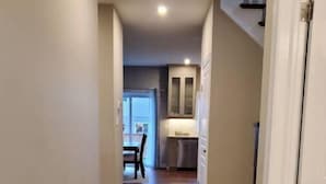 Un pasillo con piso de madera que conduce a una zona de cocina con gabinetes blancos y una encimera.