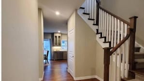 Un pasillo con suelo de madera que conduce a una escalera con barandillas blancas y pasamanos de madera.