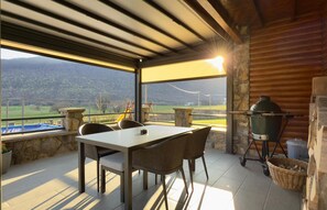 Enjoy al fresco dining with a scenic view from this outdoor dining area, featuring a table and chairs under a shaded structure with a large window offering a view of the surrounding landscape.