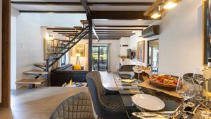 Uma sala de estar ampla com uma escada moderna, uma mesa de jantar com tampo de vidro e diversas opções de comida e bebida.