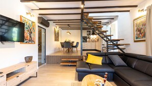 Uma sala de estar moderna com um sofá de couro preto, mesa de centro de madeira e uma área de jantar ao fundo.
