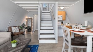 A modern kitchen with white cabinets, a dining table, and a staircase leading to an upper level. - The Bohemian A frame. (Lampe)