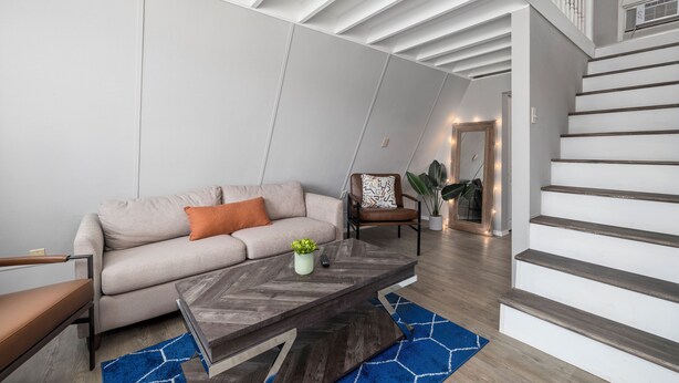 A modern living room with a sofa, coffee table, and a staircase. - The Bohemian A frame. (Lampe)