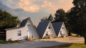 A row of two white cabins with dark roofs, each featuring a small porch and a door. - The Bohemian A frame. (Lampe)