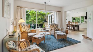 A spacious living room with wicker furniture, a round coffee table, and a view of the garden through large windows.