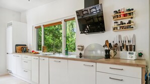A modern kitchen with white cabinets, a wooden countertop, a built-in stove, and a window overlooking greenery.