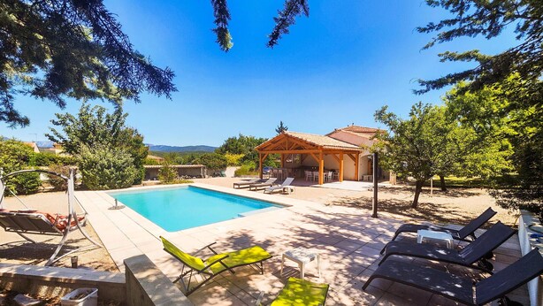 A pool area with lounge chairs, a covered seating area, and a view of the mountains.