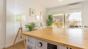 Una cocina moderna con encimera de madera, estufa integrada y zona de comedor con sillas de mimbre.