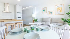 Una cocina moderna con armarios blancos, una mesa de comedor con platos y tazas, y un sofá gris en la sala de estar.