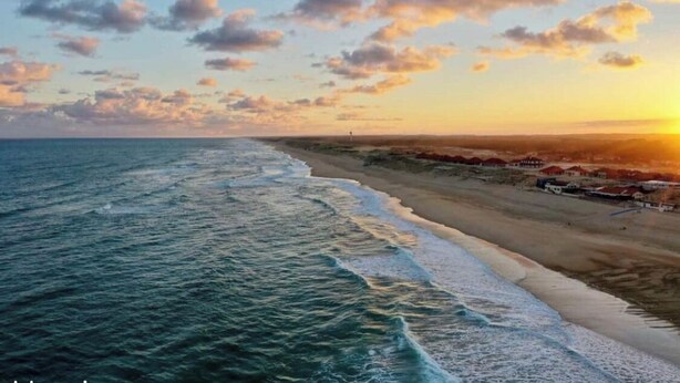 Une plage avec des vagues, un ciel dégagé et des bâtiments visibles au loin.