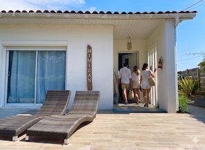 A building with a tiled roof, a large glass door, and two wicker lounge chairs. - Caporizon - Villa Cosy Proche Plage Avec Grande Terrasse (Mimizan)