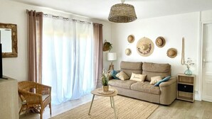 Un salon comprenant un canapé, une table basse en osier, un fauteuil, une lampe et un mur décoré de chapeaux.