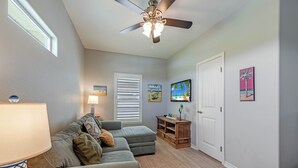A living room with a ceiling fan, a sofa, a TV, and artwork on the walls. - Bonnie Dune by Silver Sands Vacation Rentals (Port Aransas)