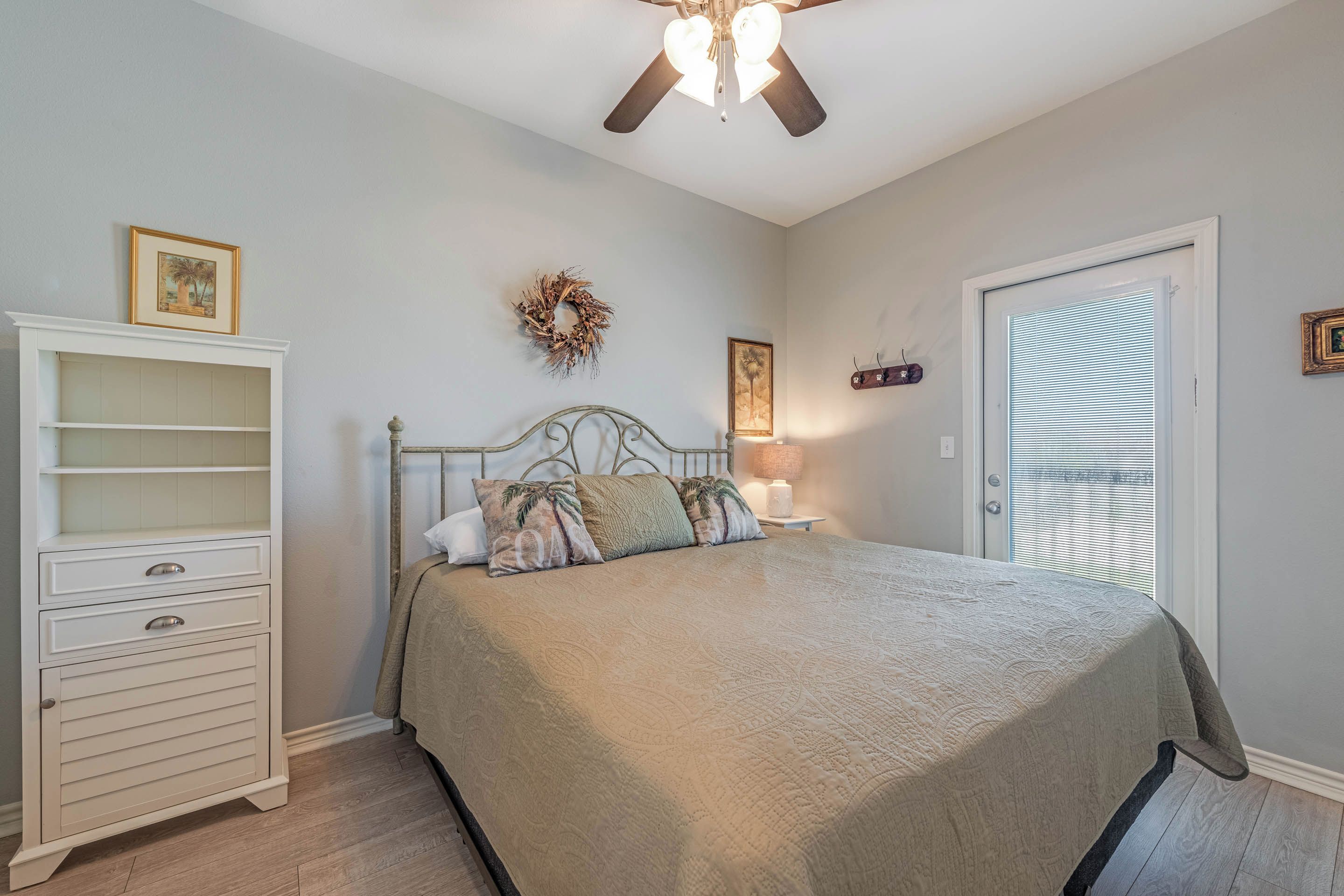 A bedroom with a bed, a nightstand, a dresser, a ceiling fan, and a door with blinds.