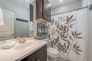 A bathroom with a white sink, dark cabinets, a toilet, and a shower curtain with a leaf pattern.