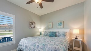 A bedroom with a bed, ceiling fan, two wall-mounted lamps, and a window with blinds. - Bonnie Dune by Silver Sands Vacation Rentals (Port Aransas)