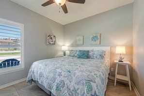 A bedroom with a bed, ceiling fan, two wall-mounted lamps, and a window with blinds.