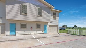 A two-story building with numbered doors, a garage, and a parking area with marked spaces. - Bonnie Dune by Silver Sands Vacation Rentals (Port Aransas)