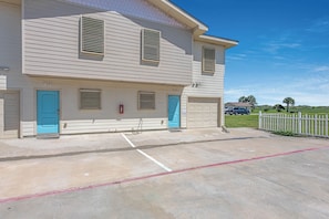 A two-story building with numbered doors, a garage, and a parking area with marked spaces.