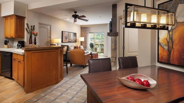 A modern kitchen with wooden cabinets, a dining area with a wooden table and chairs, and a living room with a sofa and a fireplace. - Sheraton Lakeside Terrace Villas at Mountain Vista (Avon)