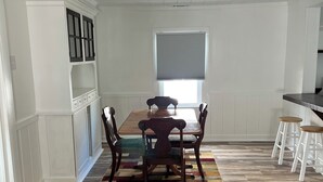 A dining area with a wooden table and chairs, a patterned rug, and a window with blinds. - The HoneyComb - Blocks from Historic Waterfront (Beaufort)