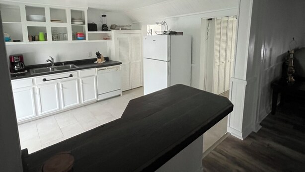 A kitchen with white cabinets, a black countertop, and a refrigerator. - The HoneyComb - Blocks from Historic Waterfront (Beaufort)