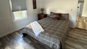 A bedroom with a large bed, a window with blinds, a nightstand, and a lamp. - The HoneyComb - Blocks from Historic Waterfront (Beaufort)