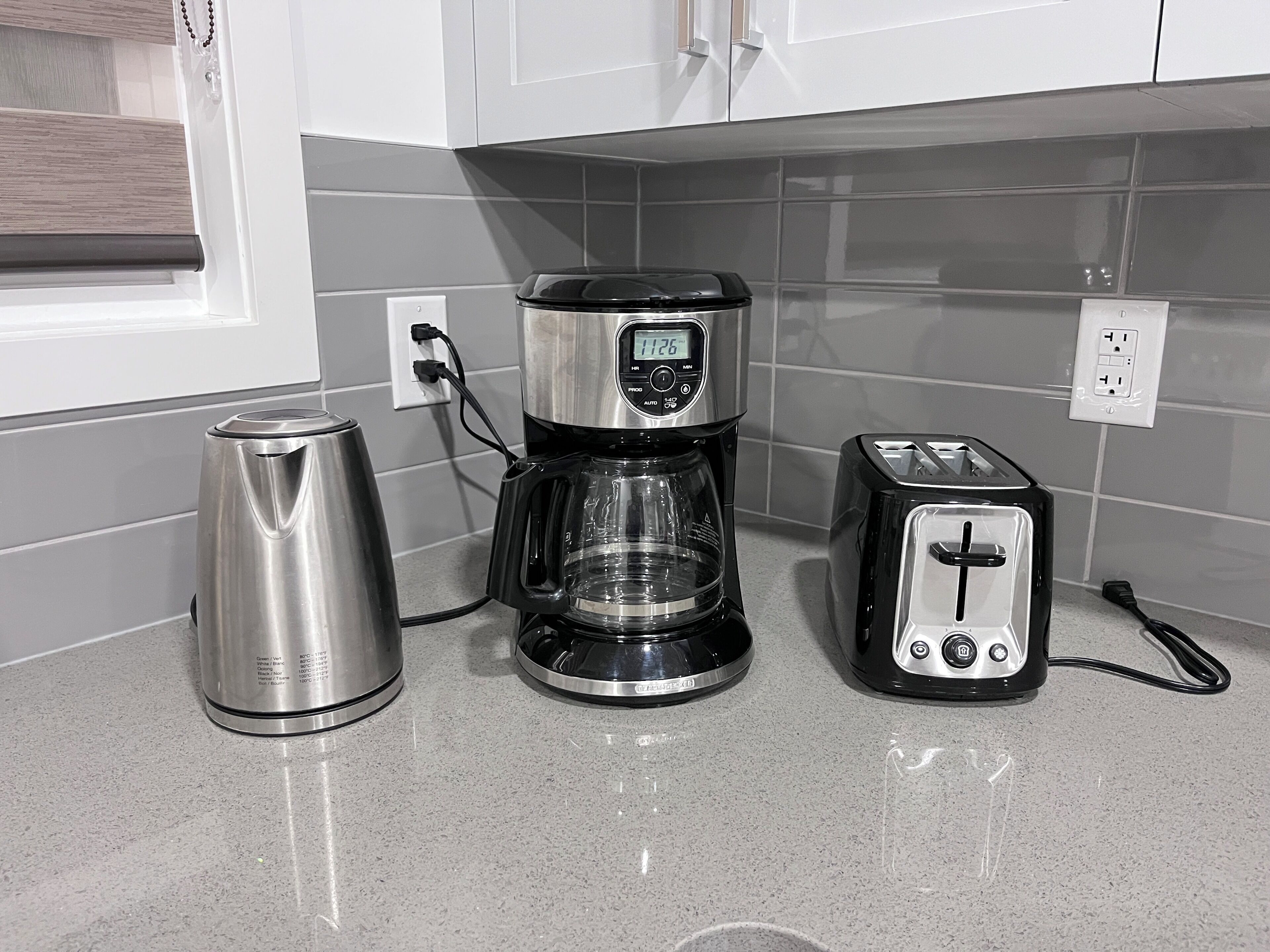 A kitchen with a coffee maker, a toaster, and a stainless steel kettle on a countertop.