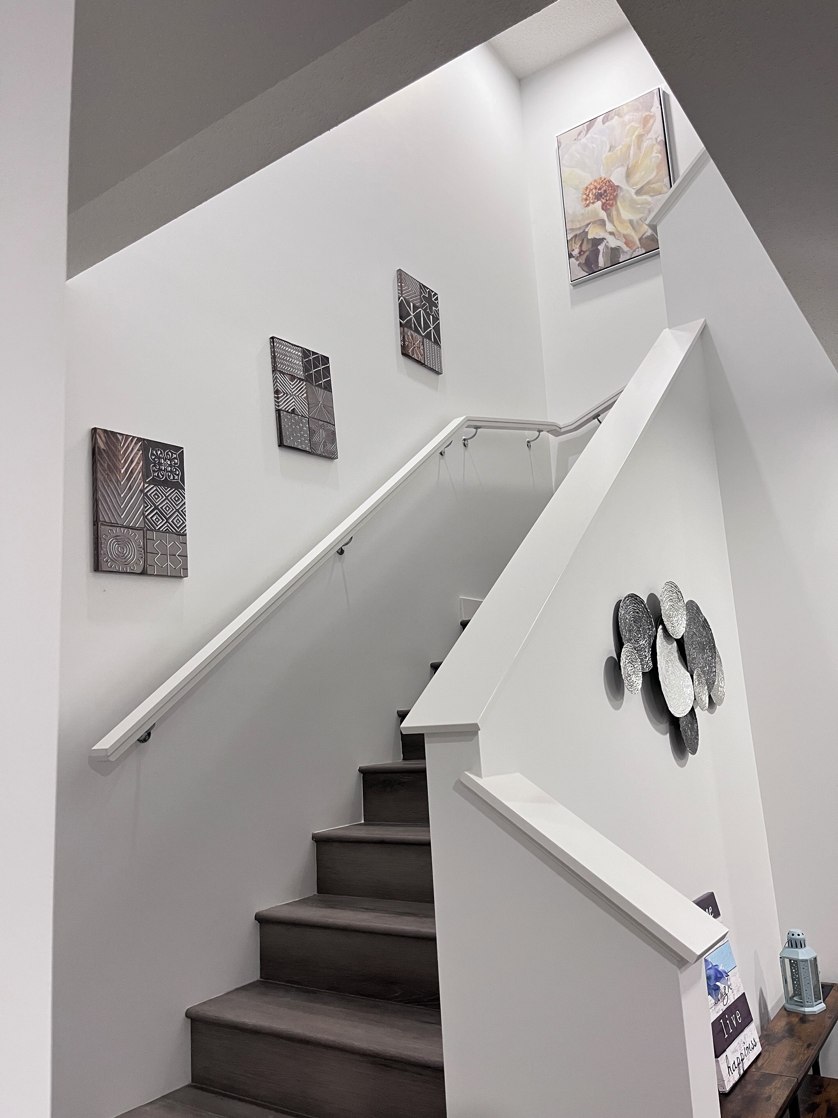 Uma escadaria com corrimão branco, degraus escuros e detalhes decorativos na parede.