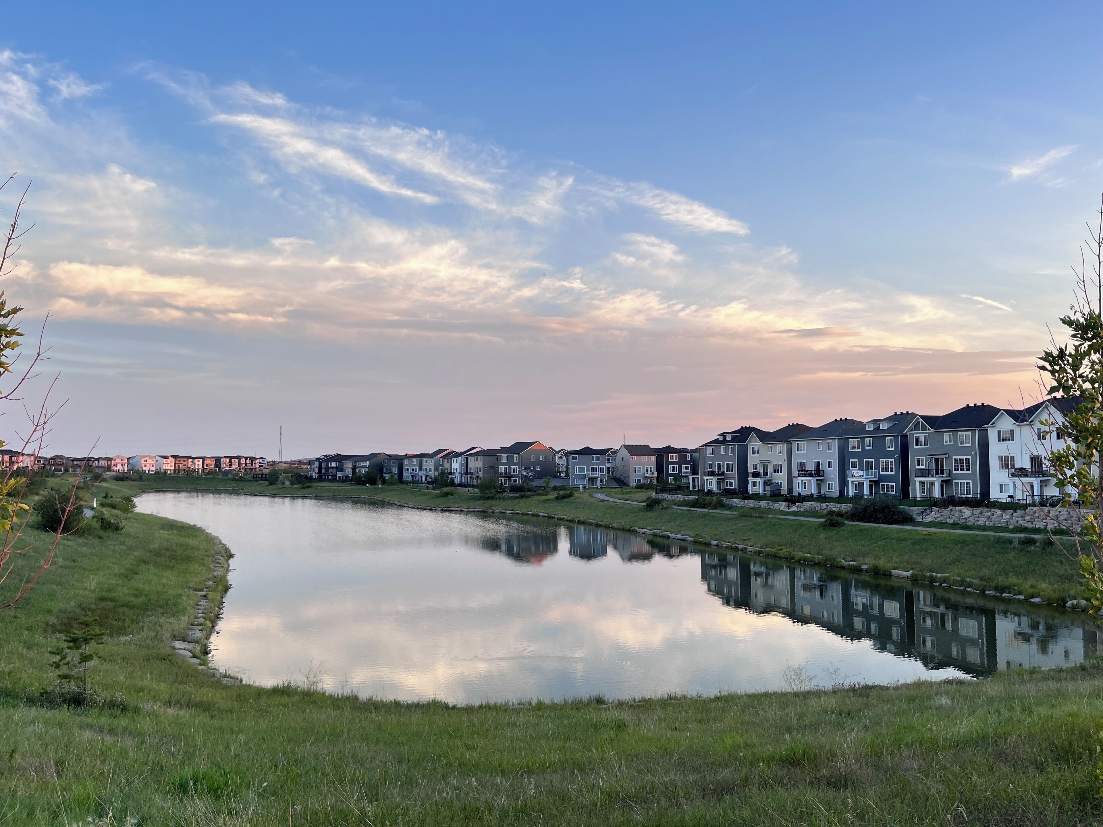 Une rangée de maisons de ville modernes, avec un lac paisible au premier plan, qui reflète les bâtiments et le ciel.