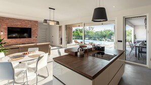 A modern kitchen with a central island, a dining area, and a large window overlooking a pool. - Cozy home in Seline with sauna (Seline)