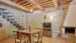 Ein rustikales Interieur mit einer Steinwand, einer Holztreppe, einem Essbereich mit Tisch und Stühlen, einem Fernseher und einem Kamin.
