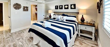 A bedroom with a large bed, a ceiling fan, and a nightstand with a lamp.