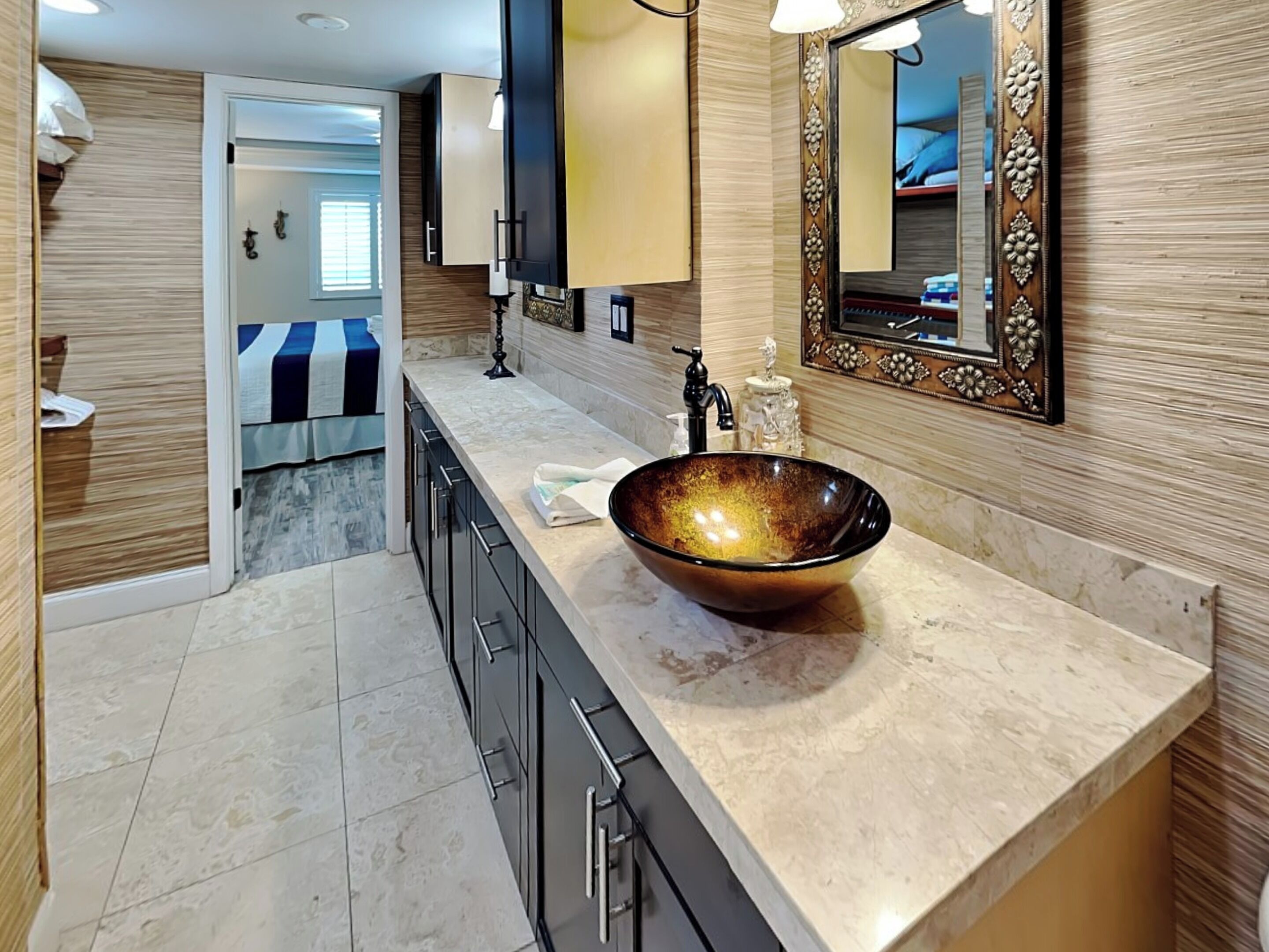 Un baño moderno con un lavamanos grande, redondo y de color oscuro, un espejo con un marco ornamentado y una encimera con una toalla.
