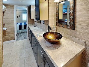 Une salle de bain moderne avec un grand lavabo rond de couleur sombre, un miroir doté d’un cadre orné et un plan de toilette sur lequel est posée une serviette.